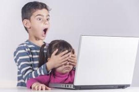 Two children are looking t the computer. Th elder on is surprised by what he saw and closed the eyes of little one. 