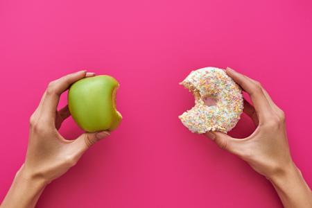 An apple in one hand and a doughnut in another hand. 