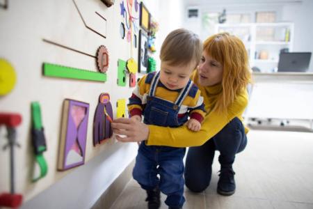 Mother and her baby son playing with wooden interactive board 