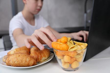Boy working using computer and eating fast food and snacks. 