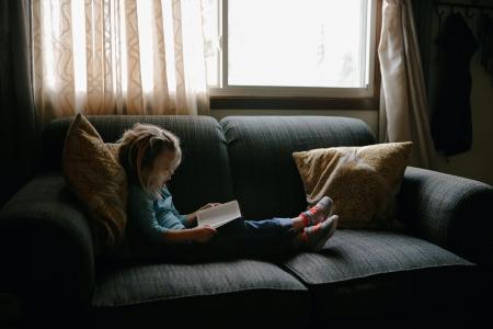 Devojčica sedi na krevetu i čita knjigu