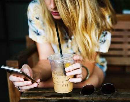 Blonde girl on a mobile phone , drinking a long iced coffee with a straw